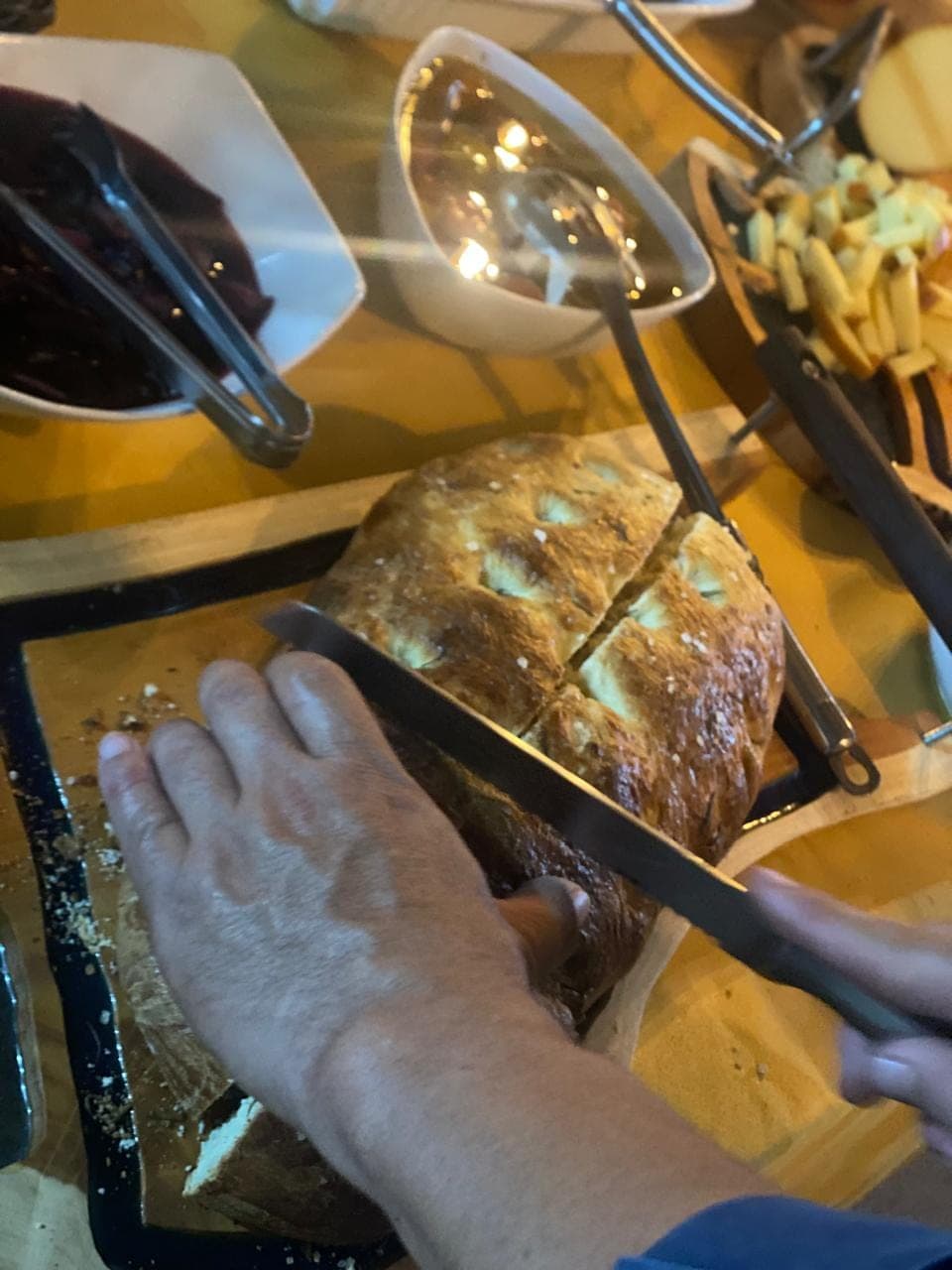 Pão rústico sendo fatiado sobre a mesa do buffet durante o evento
