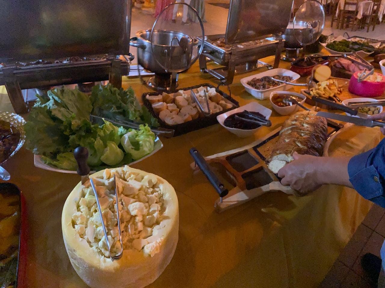 Peça inteira de queijo servida no buffet, ao lado da estação de saladas