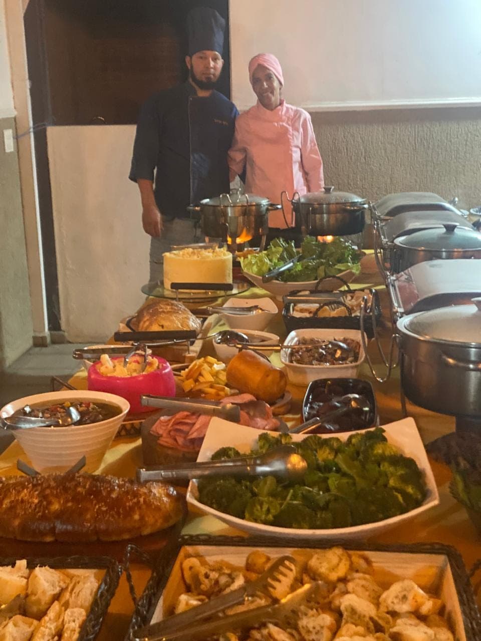 Chef Sérgio Brito ao lado de um buffet completo, com travessas de entradas e pratos quentes