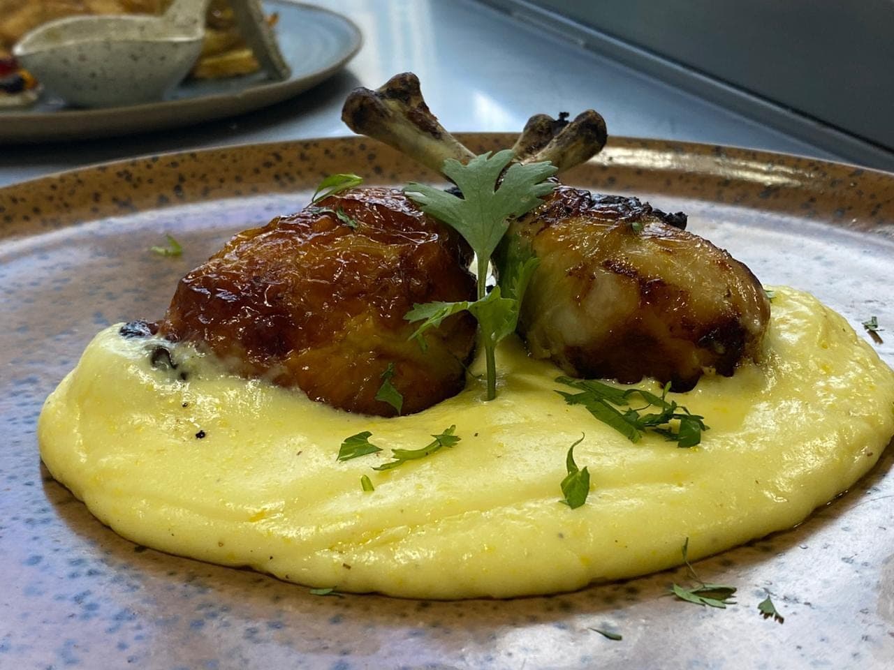 Coxa de frango confitada sobre purê, finalizada com ervas frescas