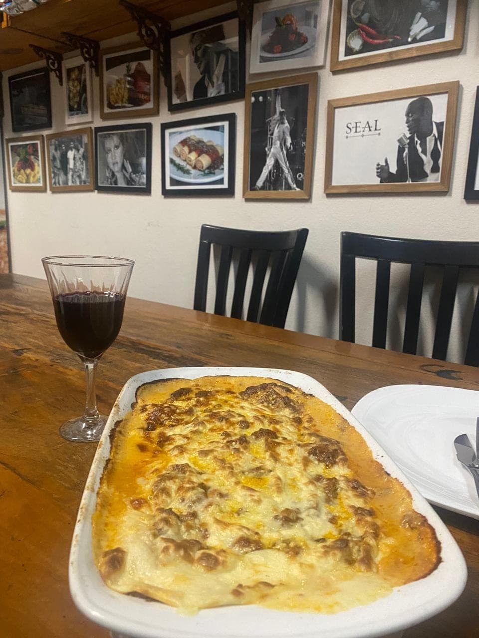 Lasanha gratinada servida à mesa, com taça de vinho ao lado