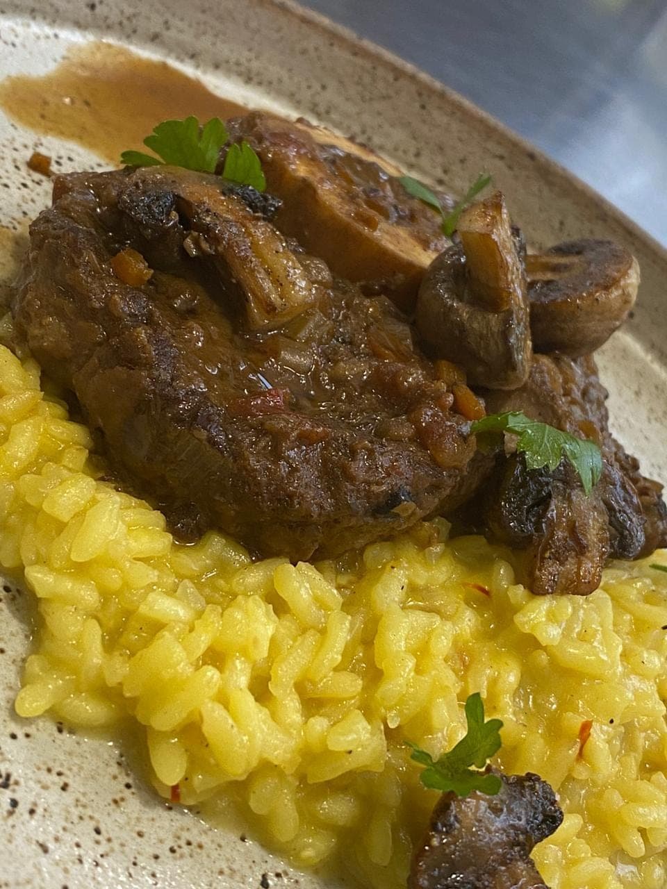 Carne braseada servida sobre risoto de açafrão com cogumelos