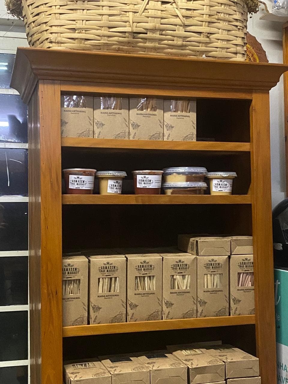 Prateleira de madeira com potes e caixas dos produtos do Armazém das Massas