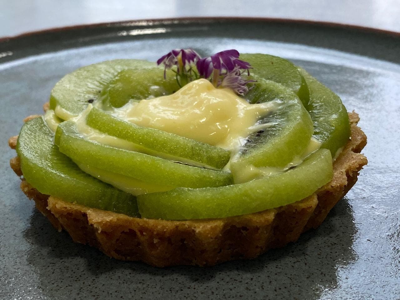 Torta de kiwi com creme e flor comestível em prato de cerâmica