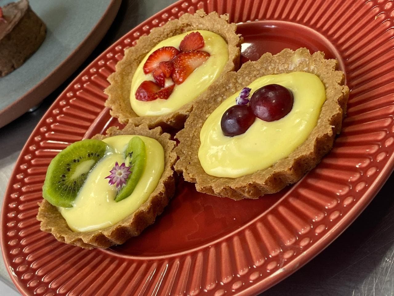 Tortelettes de creme com morango, uva e kiwi em prato vermelho
