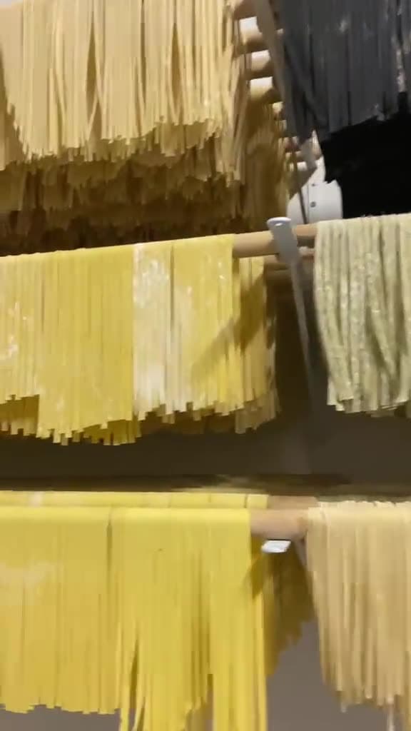 Fios de massa artesanal preta e verde pendurados no varal de secagem da cozinha de produção